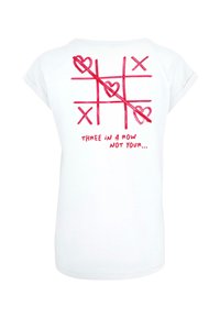 Hvit bomull t-skjorte med korte ermer, med et rosa tic-tac-toe design, hjerter, og teksten "TRE PÅ RAD IKKE DIN..." på baksiden.