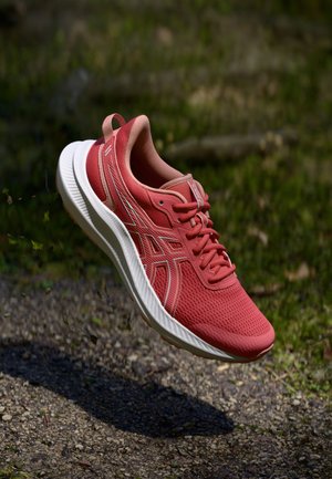 Red athletic shoe with a mesh upper, rounded white sole, and contrasting accents. Features laces and a pull tab at the heel.