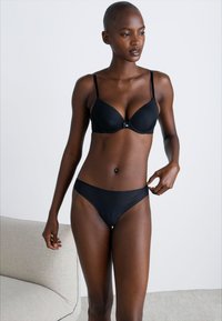 Zwarte bh en bijpassende bikini broek. Soepele stof, gevoerde cups en verstelbare bandjes op de bh; minimale bedekking onderaan.