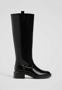 Botte en cuir noire montant jusqu'au genou avec talon bloc et languette de traction en haut, vue de profil sur un fond clair uni.