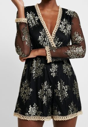 Svart jumpsuit med genomskinliga långa ärmar, guldblommönster och djup V-ringning. Har beige spetsdetaljer vid halsringningen och ärmsluten.