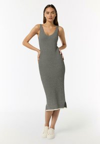 Schwarz-weiße gestreifte Midi-Kleid mit Rundhalsausschnitt, enganliegendem Schnitt,Seitenschlitzen und weichem Stricktextur, kombiniert mit weißen Sneakers.