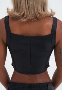 Top corto negro hecho de material suave, con escote cuadrado y una cremallera discreta en la parte posterior.