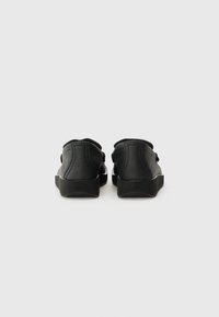Adidași din piele neagră cu un finisaj texturat, design cu profil redus și talpă din cauciuc. Prezintă un vârf rotunjit și detalii subtile de cusătură.