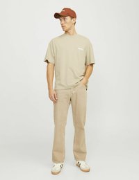Beige cotton t-shirt with short sleeves and a small white logo. Paired with light tan straight-leg jeans and white sneakers with green accents.