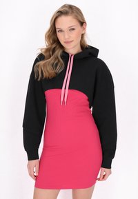 Abito con cappuccio dal top nero e parte inferiore rosa a costine. Presenta maniche lunghe e cordini a contrasto, creando un design a blocchi di colore distintivo.