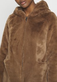 Brown faux fur jacket with a hood, featuring a zipper closure and side pockets. Soft texture and simple design.