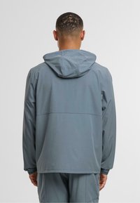 Grey hooded jacket featuring a smooth, matte texture, elastic cuffs, and a contrasting horizontal seam detail across the back.