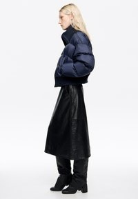 Granatowa kurtka puchowa z wysokim kołnierzem, ściągaczem u dołu, zestawiona z czarną skórzaną spódnicą i czarnymi kozakami za kolano. Gładka tekstura, dopasowany krój.