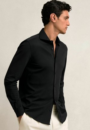 Black long-sleeve button-up shirt in smooth fabric, featuring a classic collar and fitted silhouette, paired with cream trousers.
