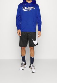 Sweat à capuche bleu avec inscription "Dodgers", short noir avec logo Nike blanc, baskets blanches et noires, chaussettes bleu marine, tenue sportive décontractée.