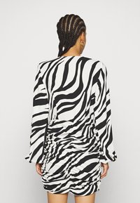 Robe à imprimé zèbre en noir et blanc, dotée de manches longues, d'un col rond et d'une texture froncée au niveau de la taille pour une silhouette ajustée.