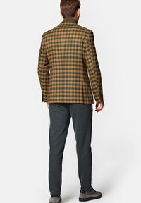 Marynarka w kratę w zielono-brązowej mieszance wełny, skrojona w dopasowanym fasonie. Połączona z ciemnoszarymi spodniami i szarymi butami.