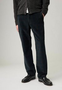 Dunkelgrüne Cordhosen für Herren mit einem dezenten Karomuster und geradem Bein. Kombiniert mit schwarzen Leder-Loafern.