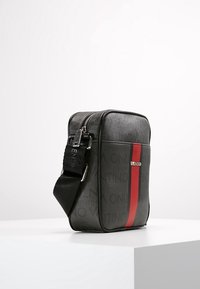 Black crossbody bag with a textured finish, featuring a prominent red stripe and silver hardware. Adjustable strap included.