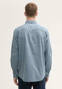 Camisa de manga larga de color azul claro con un pequeño patrón de puntos, puños abotonados y cuello con puntas; textura suave con un diseño de corte relajado.