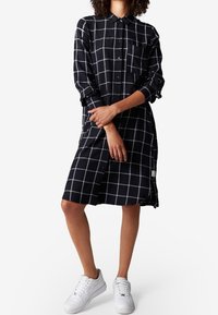 Randig svart- och vitmönstrad skjortklänning med långa ärmar, knappfront och bröstficka. Bärs med vita sneakers.