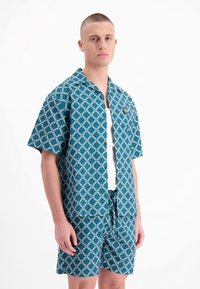 Korte mouwen blauwe shirt en bijpassende shorts met een geometrisch wit patroon. Gemaakt van lichtgewicht stof, knoopsluiting aan de voorkant, trekkoord in de taille.