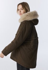 Bruine parka jas met een bontomzoomde capuchon. Heeft een gewatteerd ontwerp, lange mouwen en een getailleerde taille. Gladde stoftextuur.