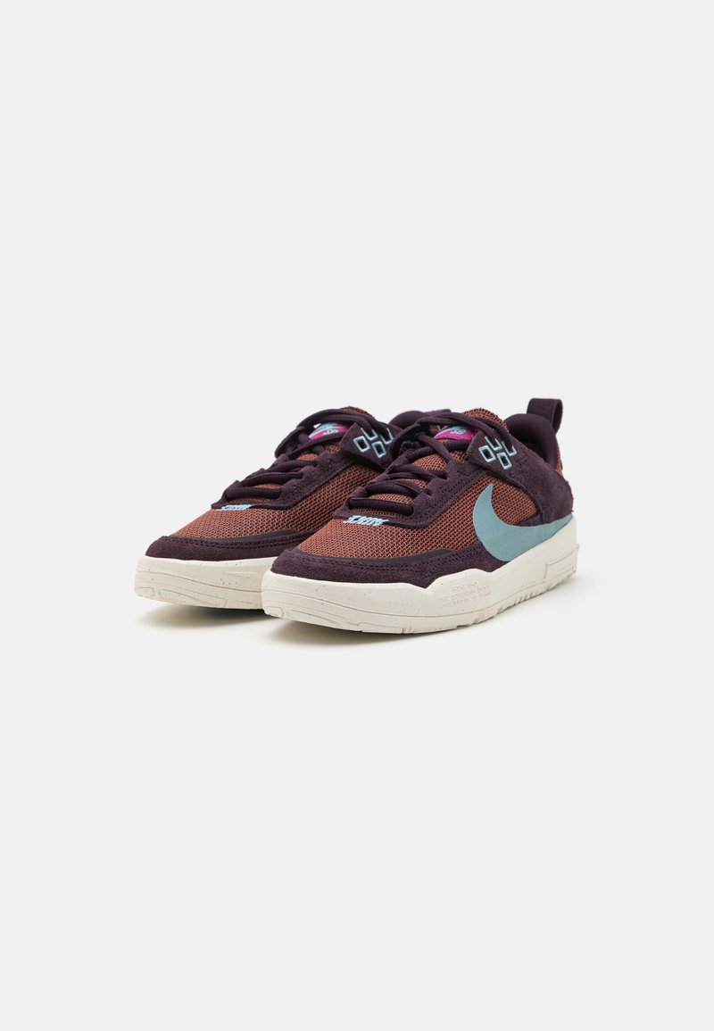 Des baskets avec une tige en mesh bordeaux et des accents en suede, un swoosh bleu clair et une semelle blanche texturée avec des éclaboussures.