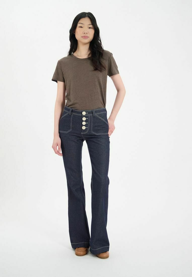 Pantalon flare en denim bleu foncé taille haute avec cinq grands boutons crème et des surpiqûres contrastées, associé à un t-shirt en coton marron.