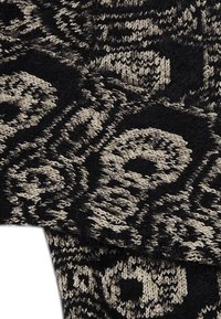 Strickstoff in Schwarz und Creme mit einem strukturierten Spiral- und Blumenmuster. Weiche, flauschige Textur mit intricaten gewebten Details.