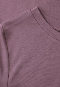 Gros plan sur le tissu d'un sweat-shirt à col rond violet doux, montrant les détails de l'épaule et de l'encolure.