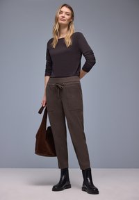 Bruin top met lange mouwen gecombineerd met donkerbruine broek met elastische taille en zijzakken, aangevuld met zwarte enkellaarzen en een bruine tote bag.