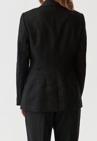 Černý lněný blazer s přiléhavým střihem, klopovými límci a rozparkem vzadu. Hladká textura s minimem švových detailů.