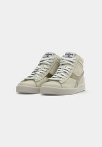 Une paire de baskets montantes blanc cassé avec des lacets blancs, une semelle texturée et une languette de marque sur un fond clair.