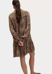 Sukienka w cętki w brązie i beżu, z długimi rękawami, ściągaczami przy mankietach i marszczonym dołem. Wykonana z lekkiego materiału.