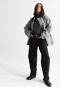 Šedý herringbone oversize kabát s černou košilí, černými širokými kalhotami a černými nazouvacími botami. Minimalistický design s uvolněným střihem.