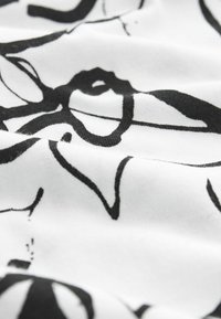 Tejido blanco con un patrón floral abstracto en negro. El diseño incluye curvas y líneas suaves sobre un fondo suave y texturizado.
