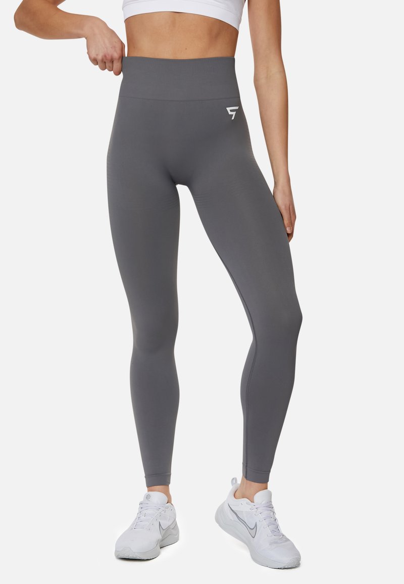 Hochgeschnittene, graue Leggings aus deastischem Material. Sie zeichnen sich durch eine glatte Textur und ein kleines weißes Logo auf der linken Hüfte aus.