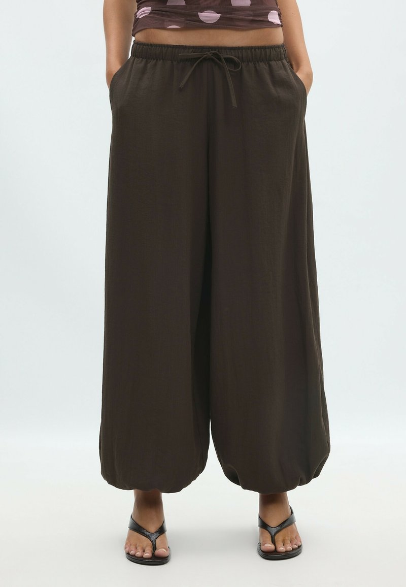 Pantalon noir ample avec taille élastique et cordon, porté avec des sandales noires à brides et un haut court à pois, visible de la taille aux pieds.
