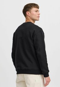 Schwarzer Sweatshirt mit gerippten Bündchen und Saum, ausgestattet mit einem Rundhalsausschnitt und einem bequemen Schnitt. Glattes Material, schlichtes Design, keine Muster.