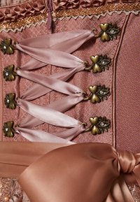 Corset rose avec laçage en satin, éléments métalliques en forme de cœur, accents floraux et motif texturé sur le tissu. Comprend un nœud en ruban de satin.