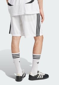 Tenue de sport avec un short blanc comportant des rayures noires sur les côtés, des chaussettes blanches avec des rayures noires, et des baskets noir et blanc avec une touche d'or.