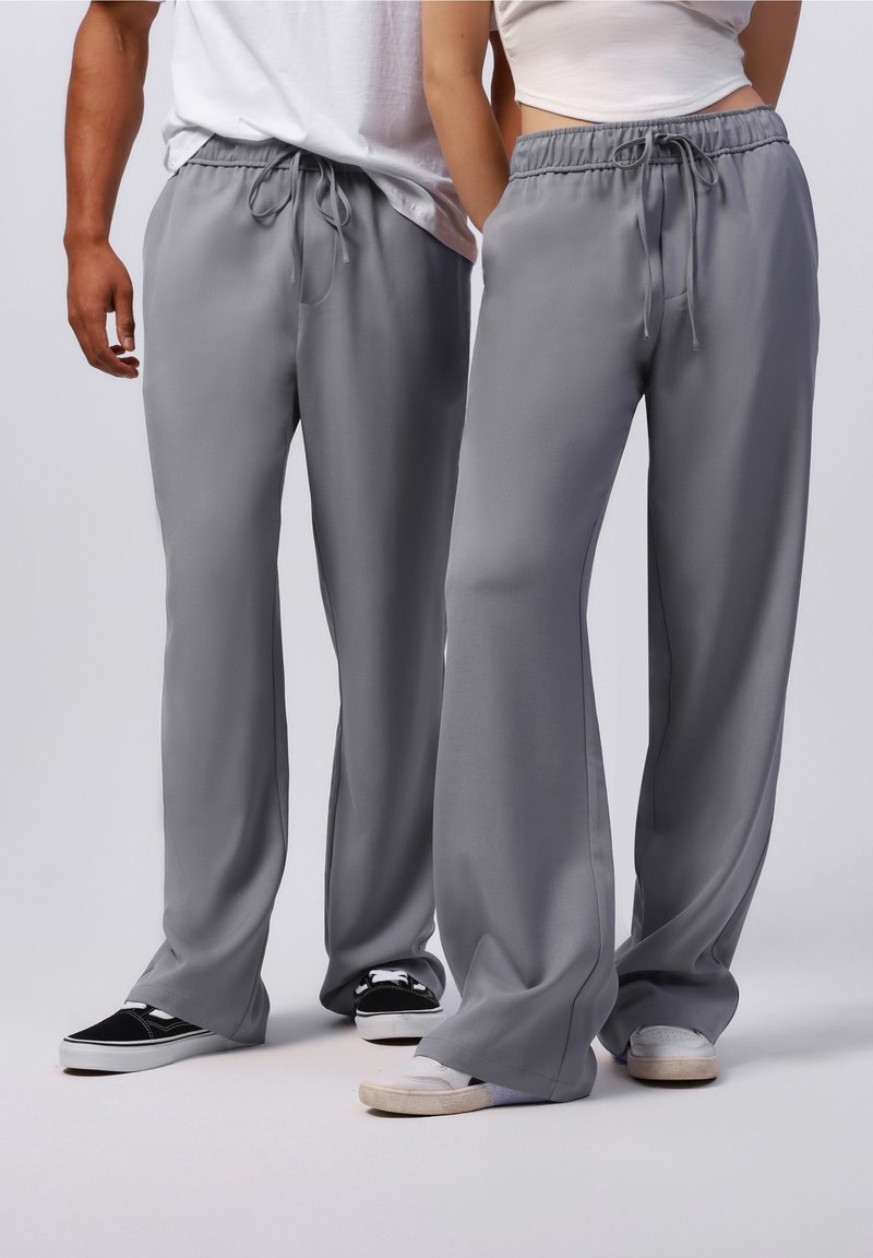 Lichtgrijze, brede broek met een trekkoord in de taille. Gladde textuur en zachte stof. Draagt met casual sneakers in contrasterende kleuren.