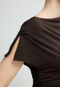 Brązowa sukienka wykonana z gładkiej, elastycznej tkaniny, z subtelnymi plisami po bokach i skośnym wycięciem na ramieniu.