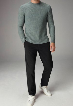 Lichtblauwe gebreide trui met textuur en geribbelde cuffs en zoom, gecombineerd met zwarte rechte broek en witte sneakers.