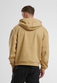Felpa beige con un ampio cappuccio morbido, polsini e orlo a costine, con una vestibilità rilassata e tessuto testurizzato. Senza logo o motivi visibili.