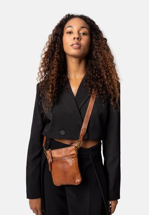 Bruine leren schoudertas met een gestructureerd oppervlak, voorzien van een rits en een afneembare schouderriem. Draagt over een zwarte cropped blazer.