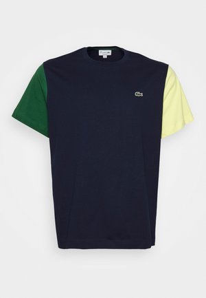 Marineblå T-shirt med korte ærmer med grøn venstre ærme, lysegult højre ærme, rund halsudskæring og lille broderet grønt krokodillelogo på brystet.