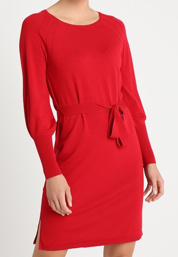 Robe rouge en tricot avec manches longues, encolure arrondie et taille cintrée par une ceinture. Comprend des fentes latérales et une texture douce et lisse.