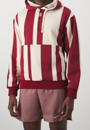 Man met een rood-wit gestreepte hoodie met trekkoorden en mauve Nike-shorts met logo op het linkerbeen.