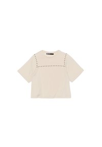 Camiseta de manga corta color crema hecha de una tela suave, con una línea horizontal de pequeños adornos con tachuelas en el pecho y un corte relajado.