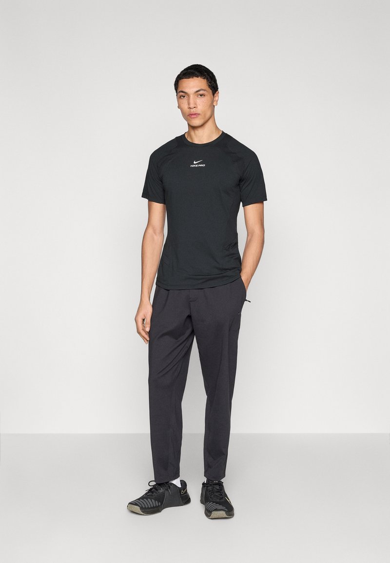 Black Nike Pro short-sleeve shirt with a fitted design, paired with dark gray pants. Model wears black athletic shoes with textured soles.