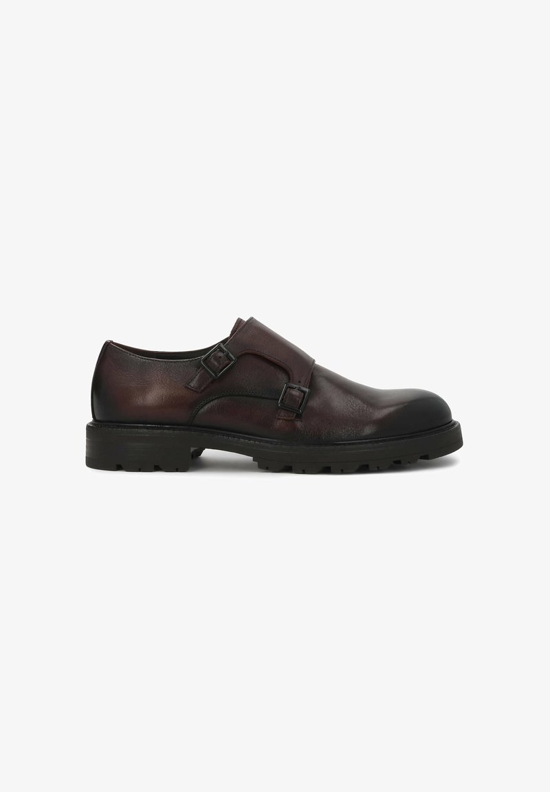 Chaussure monk strap en cuir marron foncé avec fermetures à double boucle et semelle épaisse en caoutchouc noir à profondes rainures, vue de profil sur fond blanc.