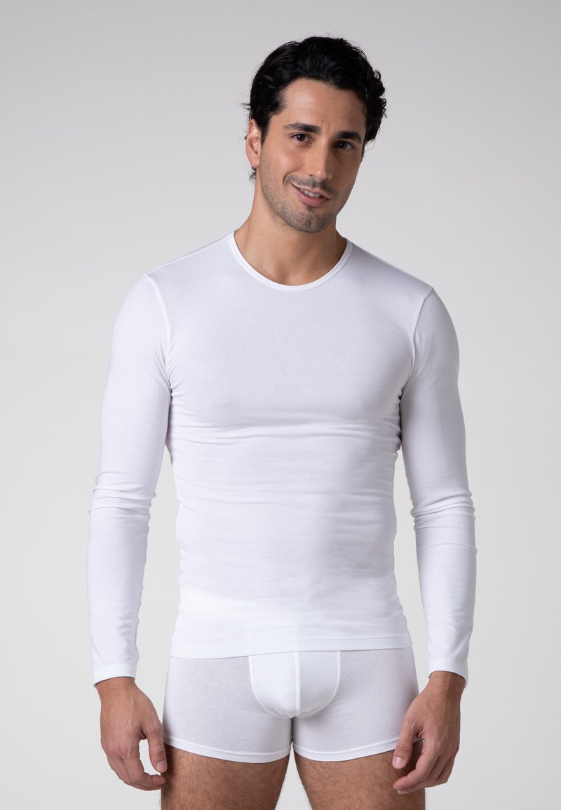 Camicia bianca a maniche lunghe e boxer bianchi realizzati in tessuto morbido. La camicia ha un collo rotondo e un design aderente.